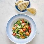 A blue and white bowl filled with melon and avocado salad with a bowl of pita beside it.