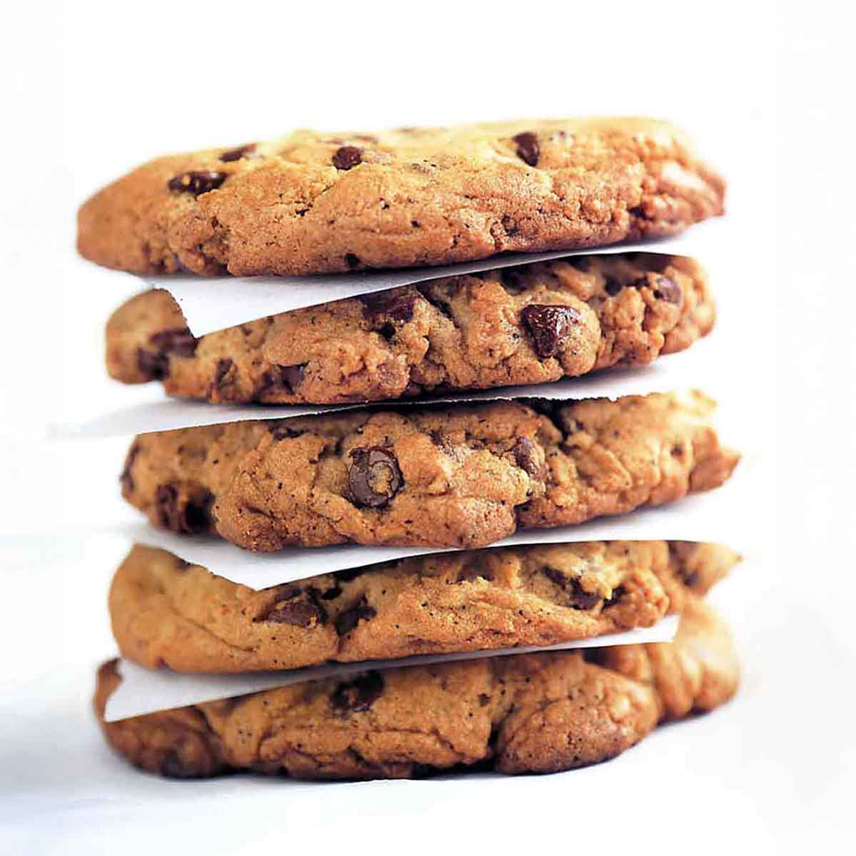 A stack of Neiman Marcus chocolate chip cookies separated by pieces of parchment.