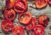 Halved slow roasted tomatoes on a piece of parchment with drops of oil and flakes of salt.