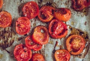 Halved slow roasted tomatoes on a piece of parchment with drops of oil and flakes of salt.