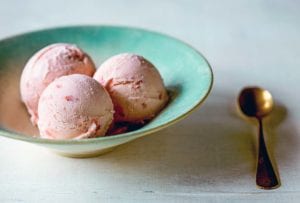 A gold-rimmed blue bowl with three scoops of strawberry buttermilk ice cream and a gold spoon beside it.