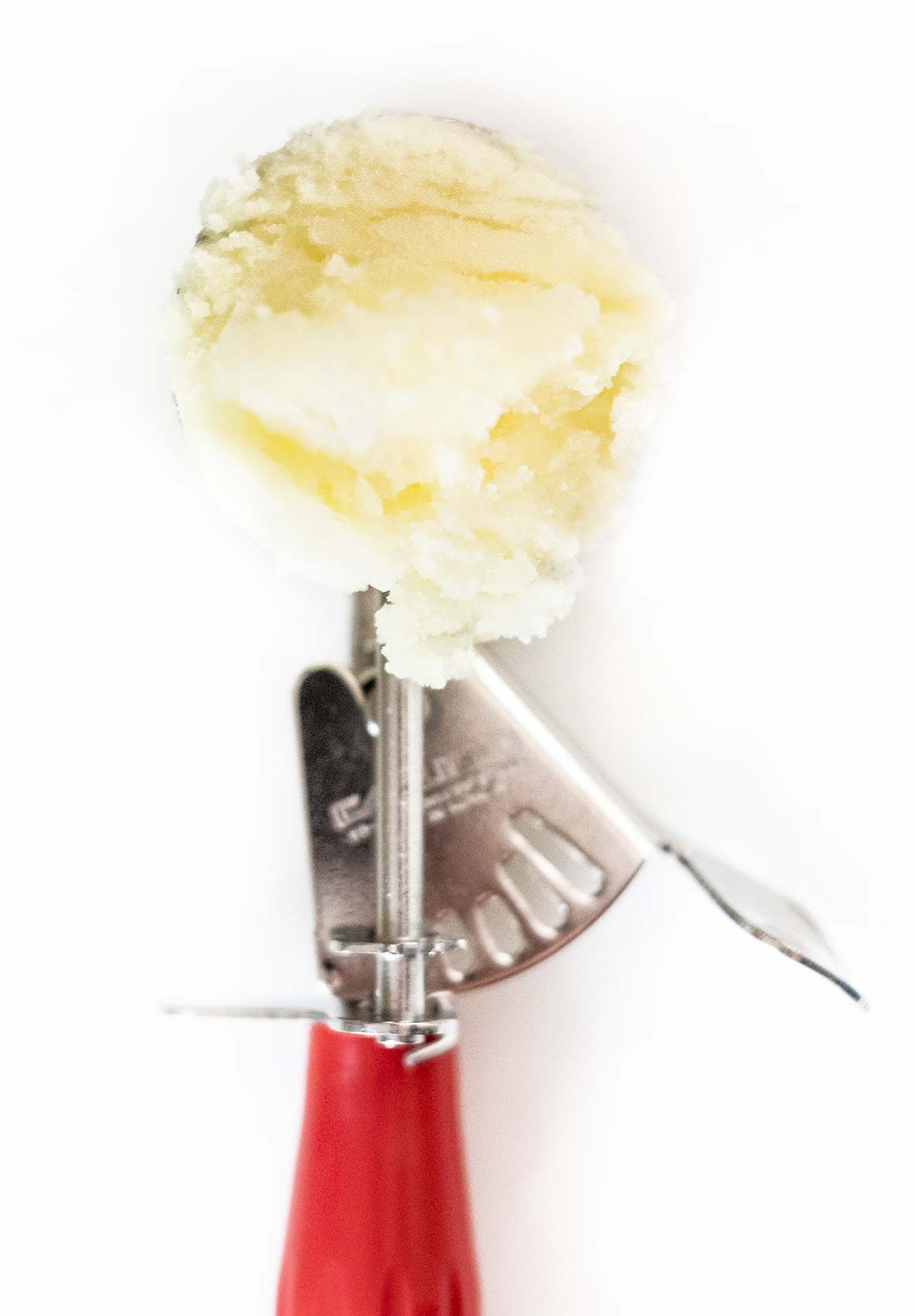 An ice cream scooper with a red handle filled with Tart Lemon Sorbet.