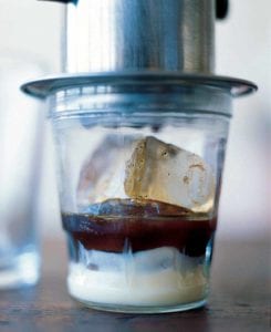 A glass of Vietnamese iced coffee, made with layers of sweetened condensed milk, coffee, and ice cubes with a coffee drip over it.