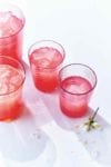 Four glasses partially filled with watermelon lemonade and topped with ice cubes.