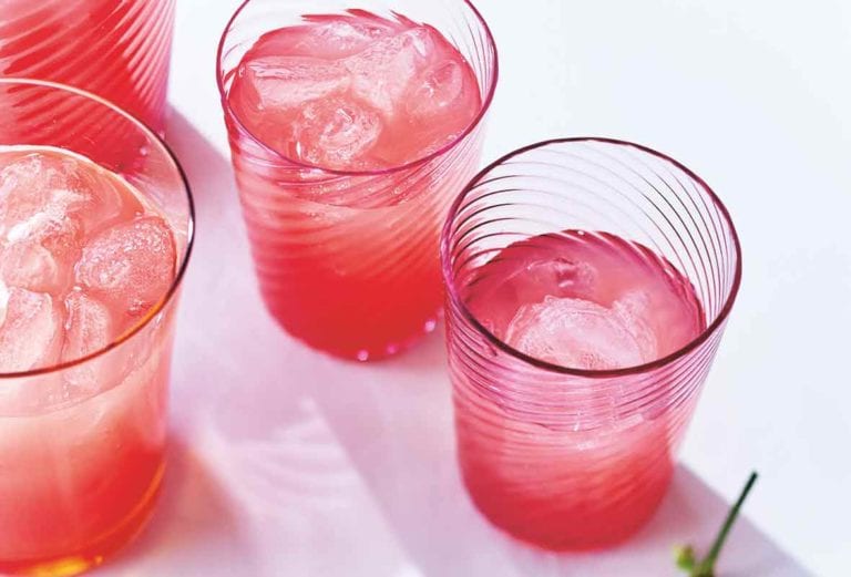 Four glasses partially filled with watermelon lemonade and topped with ice cubes.