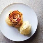 An apple rose tart, shaped to look like a rose with a scoop of ice cream beside it on a white plate.