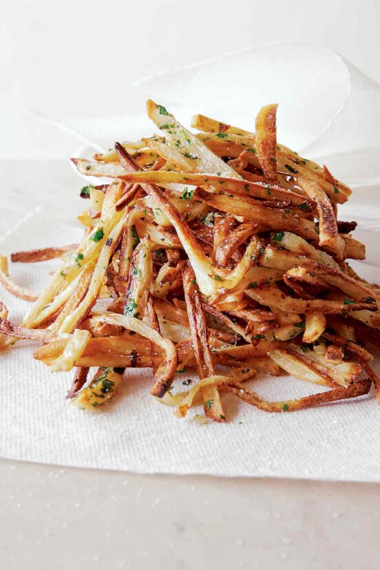 A pile of baked french fries, sprinkled with salt and fresh parsley on a paper towel.