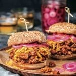 Two bourbon sloppy joes on sesame buns, topped with shredded Cheddar cheese, and pickled red onion.