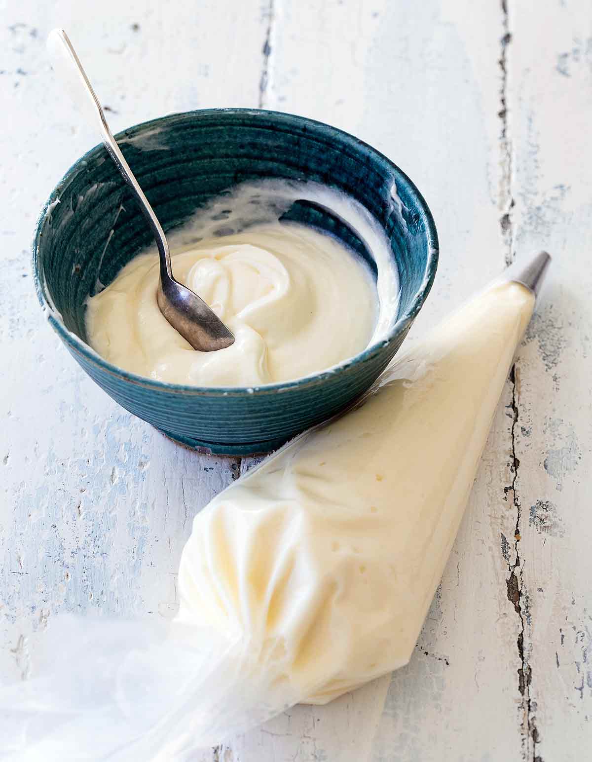 A blue bowl half filled with cream cheese frosting and a piping bag filled with cream cheese frosting beside it.