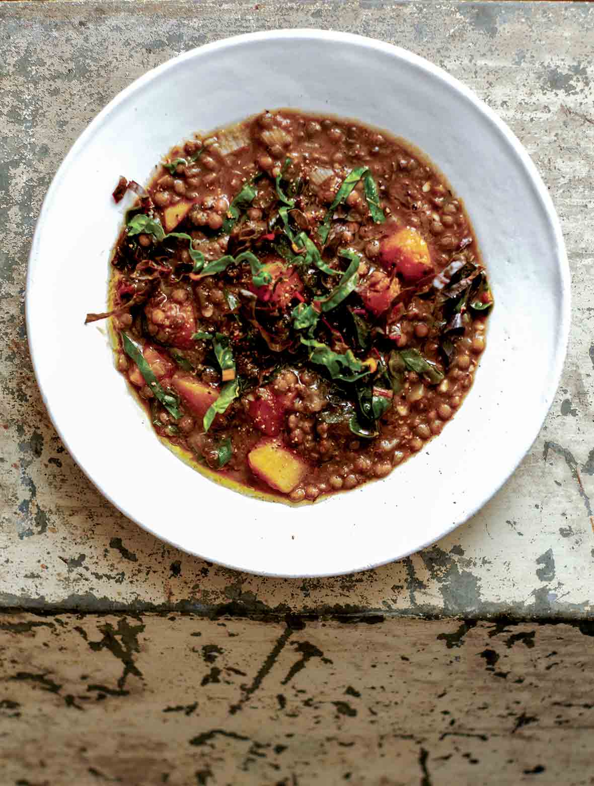 A white bowl of French lentil soup, topped with ribbons of chard.