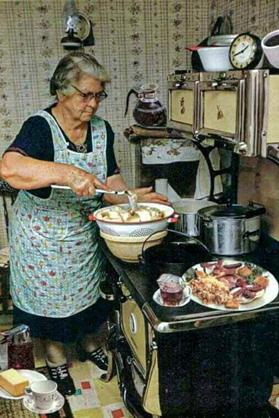 A grandmother wearing an apron cooking her kitchen with yellow cabinets.