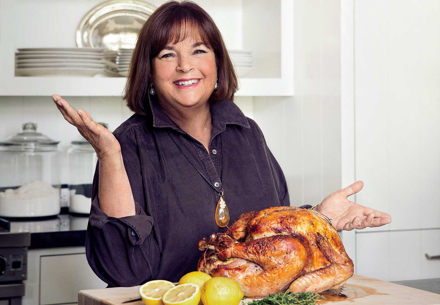 A photo of Ina Garten in her kitchen with a perfectly roasted turkey with halved lemons on her kitchen counter.