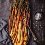 Maple glazed carrots with bourbon and parsnips on a black oval platter with a dish of salt beside it.