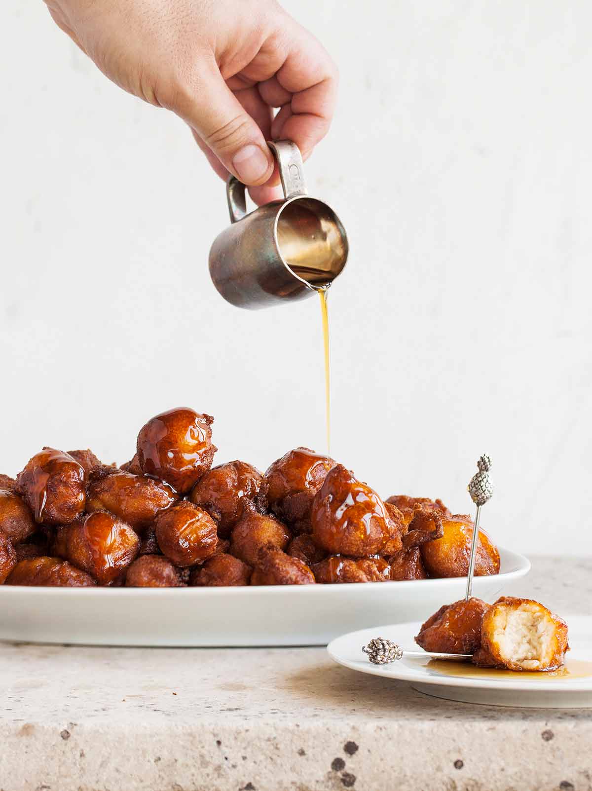 A person pouring spicy maple bourbon syrup over a platter of waffle fried chicken bites, with a white plate with two bites on it beside the platter.