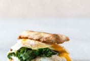 A breakfast sandwich with fried egg, kale, and ricotta sandwiched between two toasted English muffin halves.