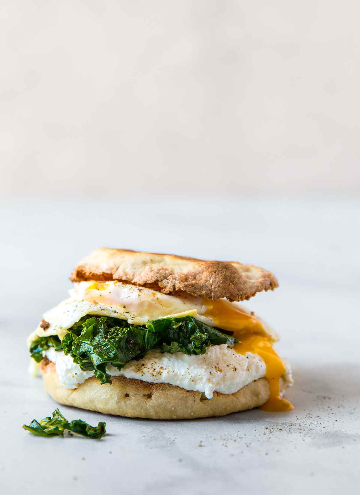 A fried egg, kale, and ricotta breakfast sandwich sandwiched between two toasted English muffin halves.