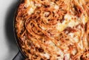 A cheesy baked spaghetti casserole in a cast-iron skillet.