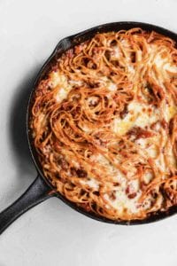 A cheesy baked spaghetti casserole in a cast-iron skillet.