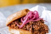 Korean-style sloppy joes made with shredded beef, topped with pickled red onion on a hamburger bun resting on a piece of parchment.