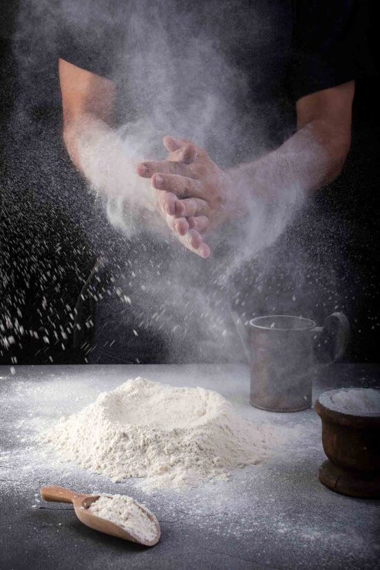 A man in a black shirt clapping the flour off his hands.