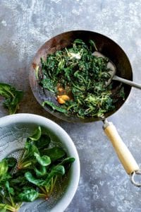 A wok filled with stir-fried spinach with miso and ginger and a colander with fresh spinach beside the wok.
