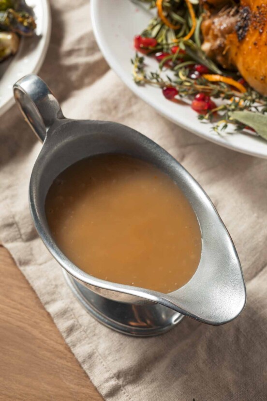 A silver gravy boat filled with gluten-free gravy on a linen cloth.