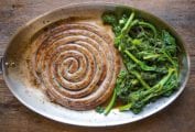 A large coil of Italian sausage and broccoli rabe in an oval skillet.