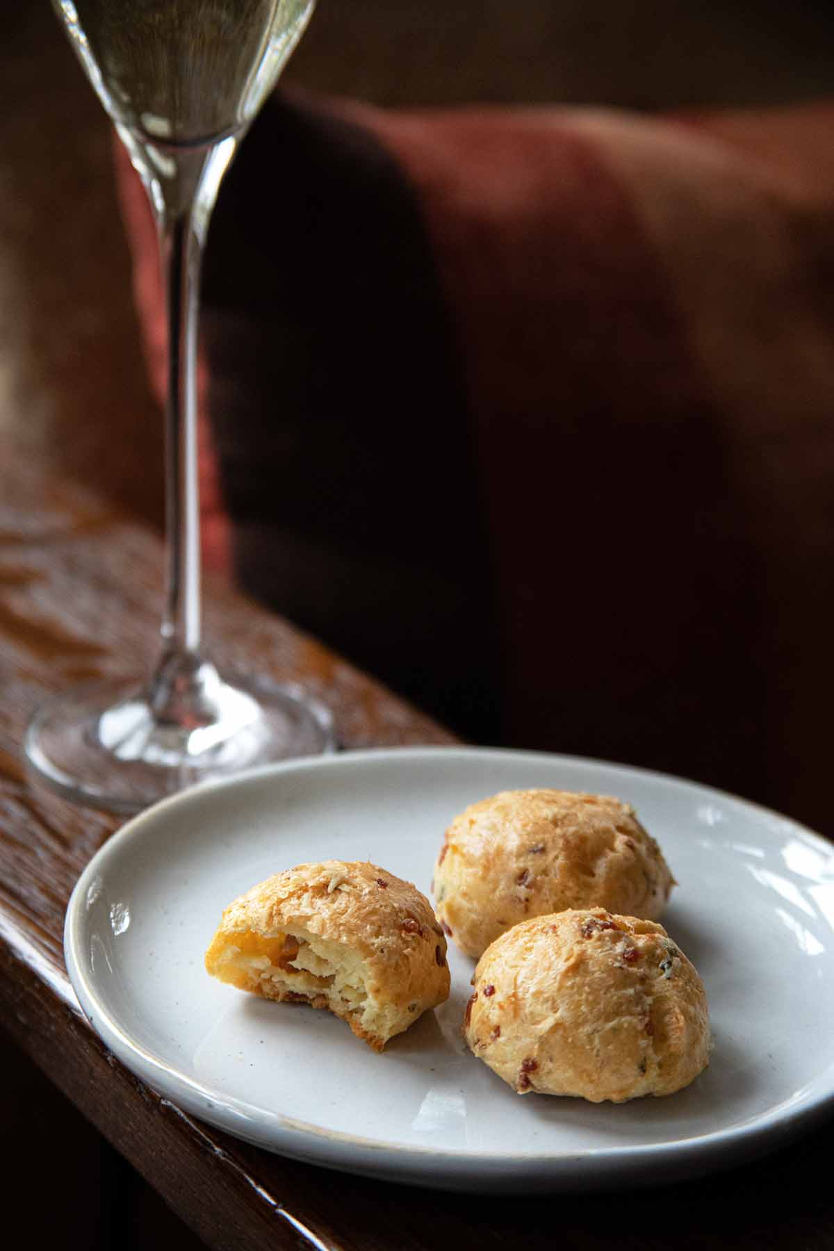 A white plate with three prosciutto-Grana Padano gougeres with a glass of Prosecco in the background.