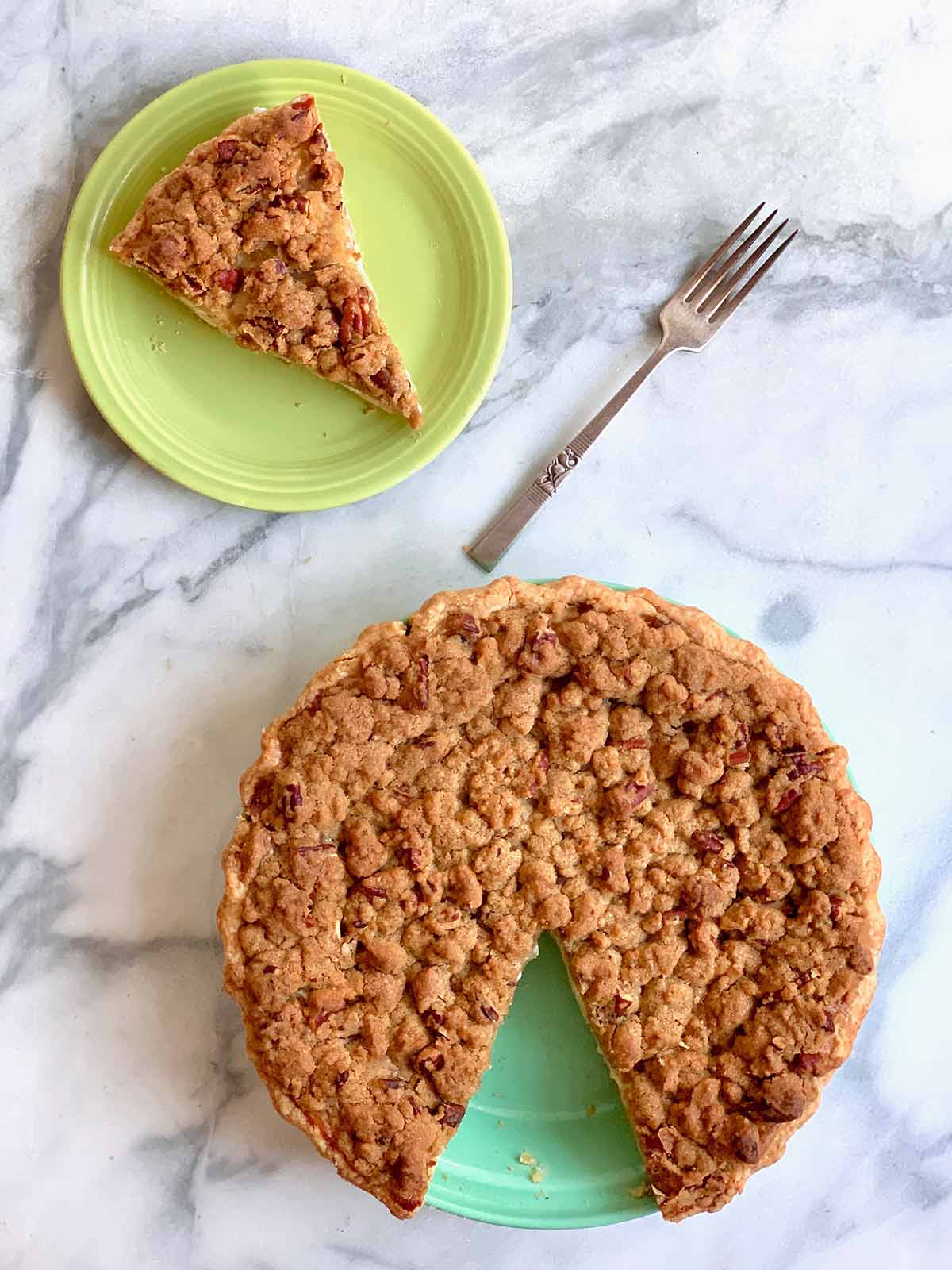 A sour cream apple pie with one slice cut out and place on a green plate and a fork resting beside it.