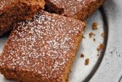 Squares of best homemade gingerbread cake dusted with confectioners' sugar on a silver platter.