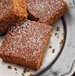 Squares of best homemade gingerbread cake dusted with confectioners' sugar on a silver platter.