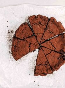 A flourless chocolate chile cake cut into 8 wedges with one slice missing on a piece of parchment paper.