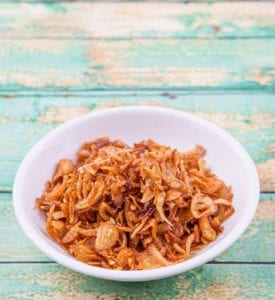 A white bowl filled with crispy fried shallots on a blue wooden surface.