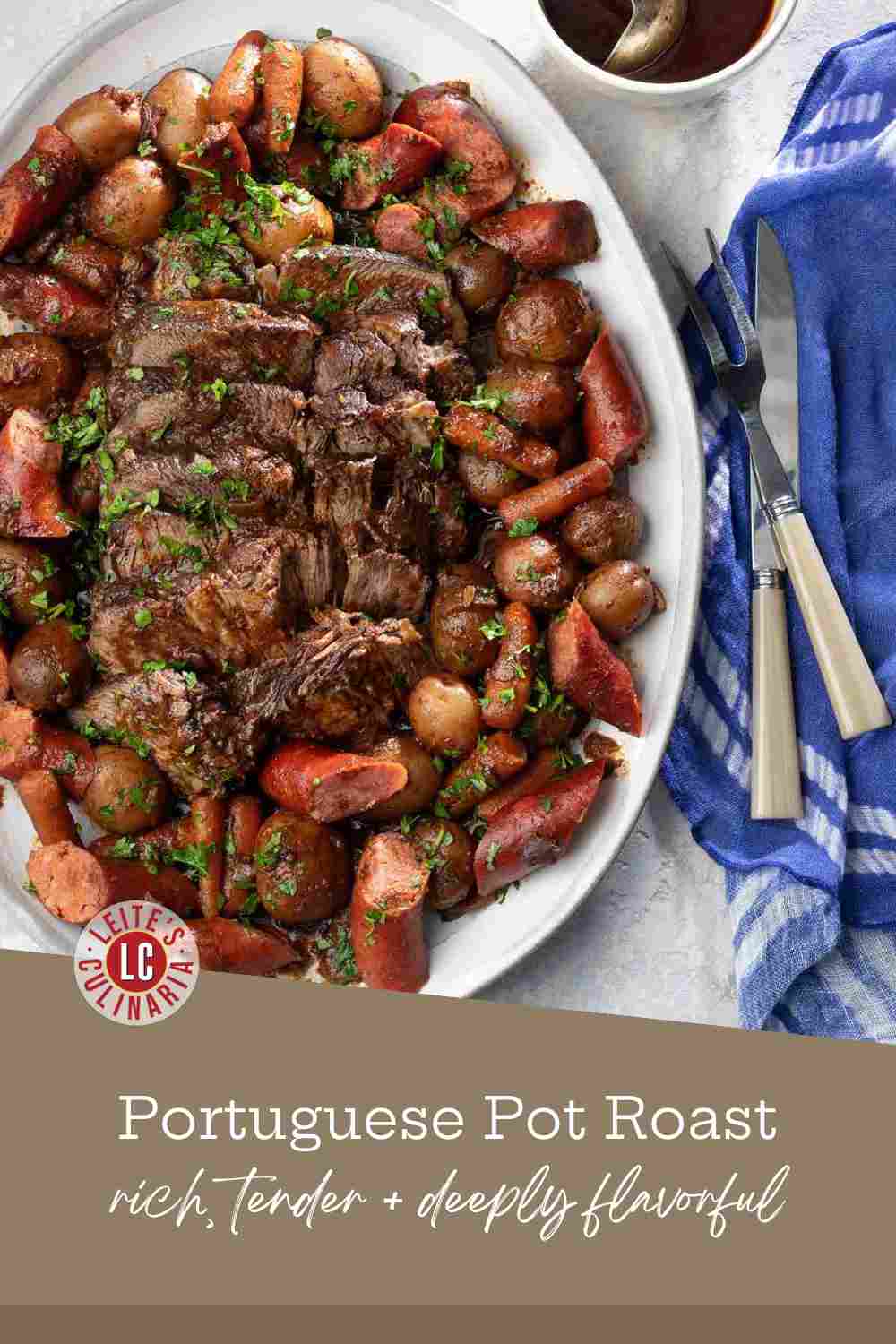 A platter of sliced braised beef surrounded by roasted potatoes, carrots, and chouriço sausage, with a side of sauce.