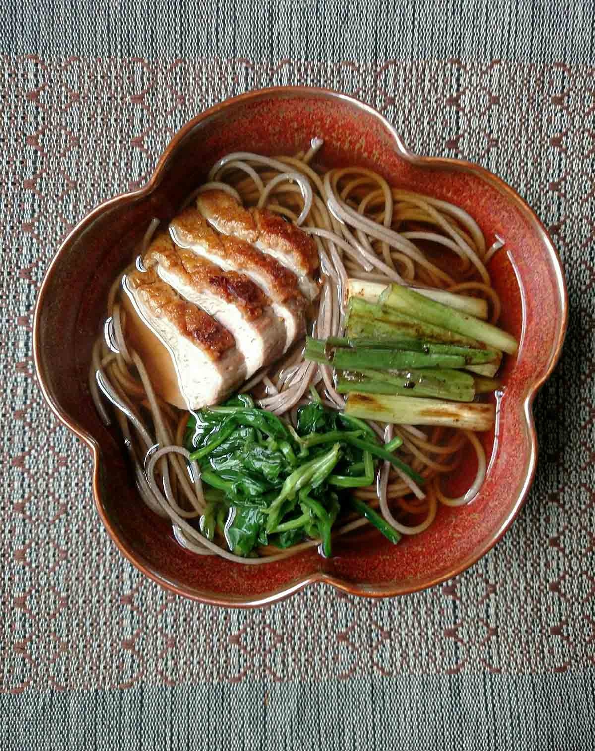 A bowl filled with duck soba, seasoned spinach, and scallions.