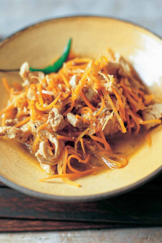 A brown bowl filled with ginger and carrot stir-fry on a wooden mat.