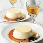 Two shallow bowls, each with an unmolded panna cotta in caramel, with a spoon resting in the bowl.