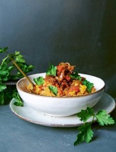 A bowl filled with spicy harissa lentil stew on a white plate with flat leaf parsley garnishing the dish and scattered around the bowl.