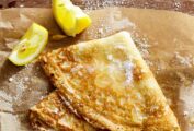 A single basic crepe, folded into quarters on a sheet of parchment with two lemon wedges beside it.