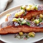 Two pieces of blackened salmon topped with pineapple salsa on an oval serving plate.