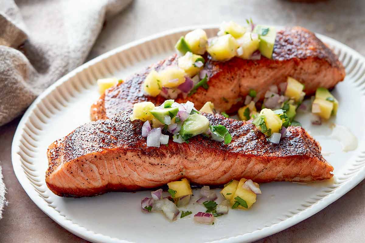 Two pieces of blackened salmon topped with pineapple salsa on an oval serving plate.