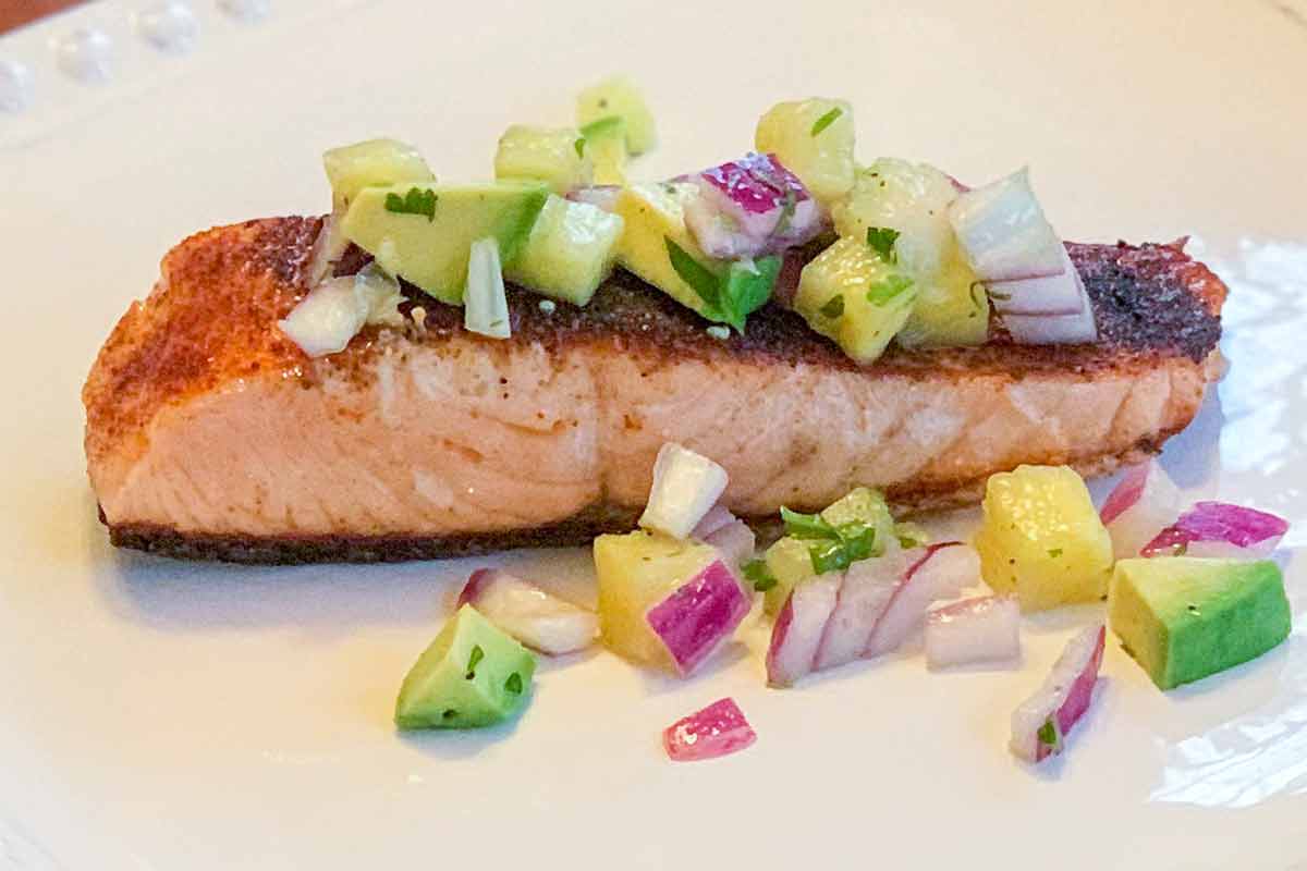 A piece of blackened salmon topped with pineapple salsa on an oval serving plate.