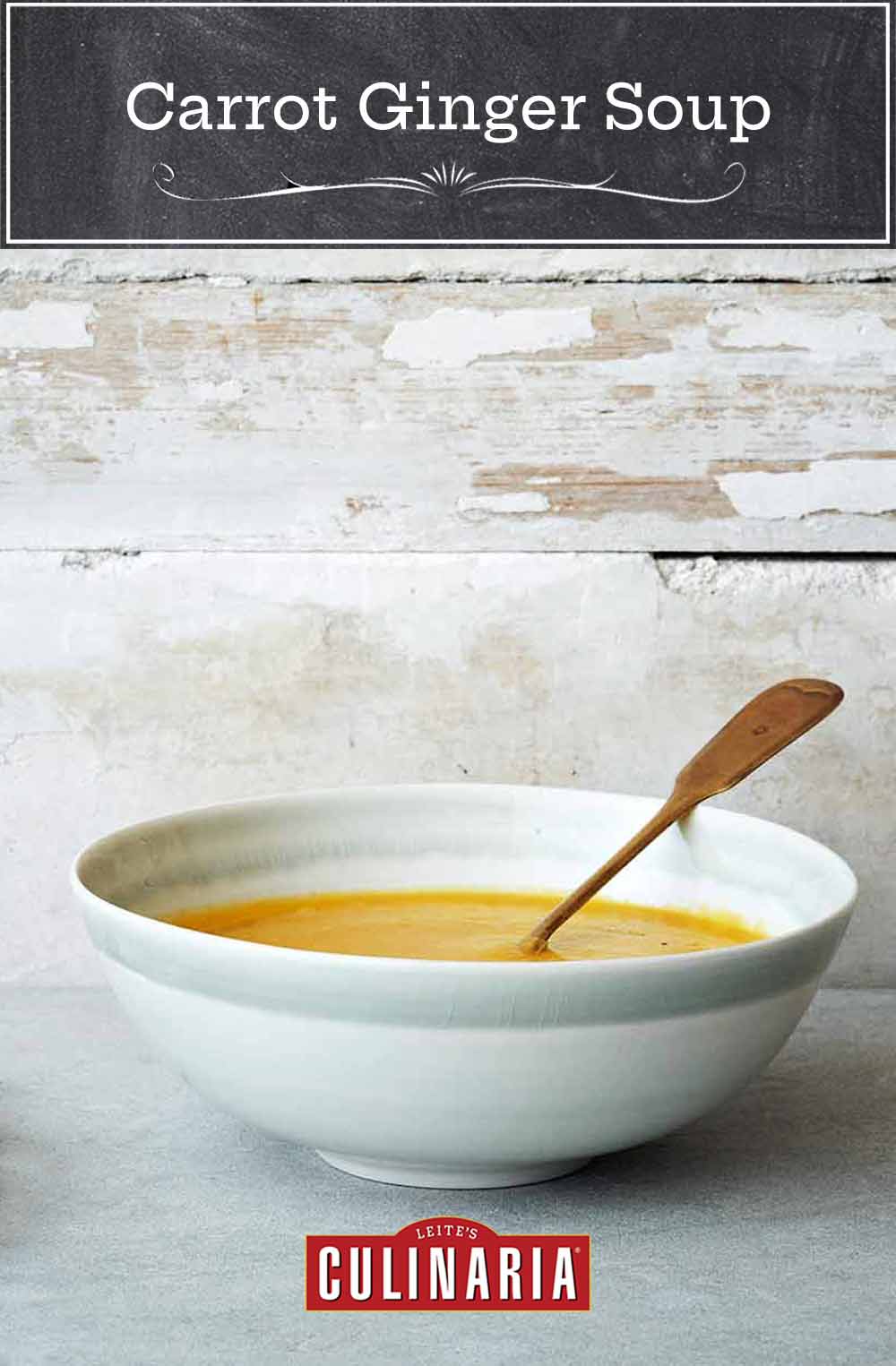 A white bowl filled with carrot ginger soup, with a spoon resting inside and a plate of carrots beside it.