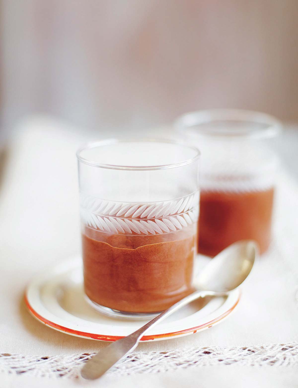 Two individual servings of chocolate mouse in glass tumblers served on a small plate with a silver spoon resting beside.