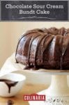 A chocolate glazed chocolate bundt cake sitting atop a white cake stand with a dish of glaze on the side