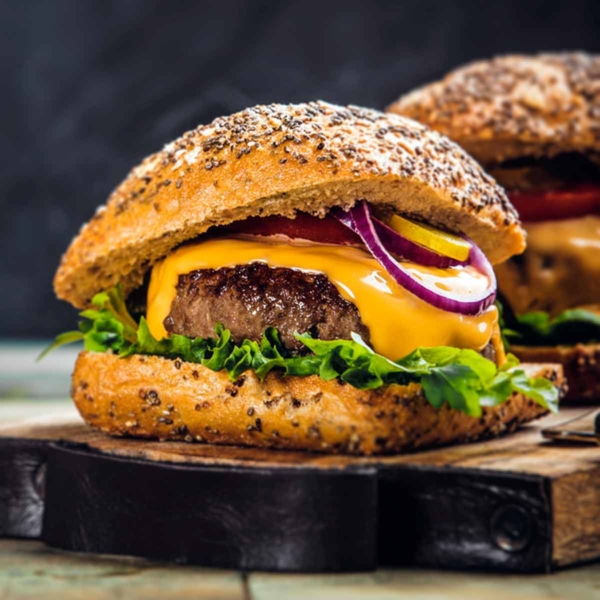 Two cheeseburgers with red onion, lettuce, and pickles on sesame buns on a wooden serving board.