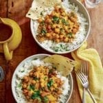 Two bowls of rice and curried chickpeas (chana masala) with two forks and a yellow cloth on the side.