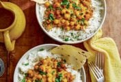 Two bowls of rice and curried chickpeas (chana masala) with two forks and a yellow cloth on the side.