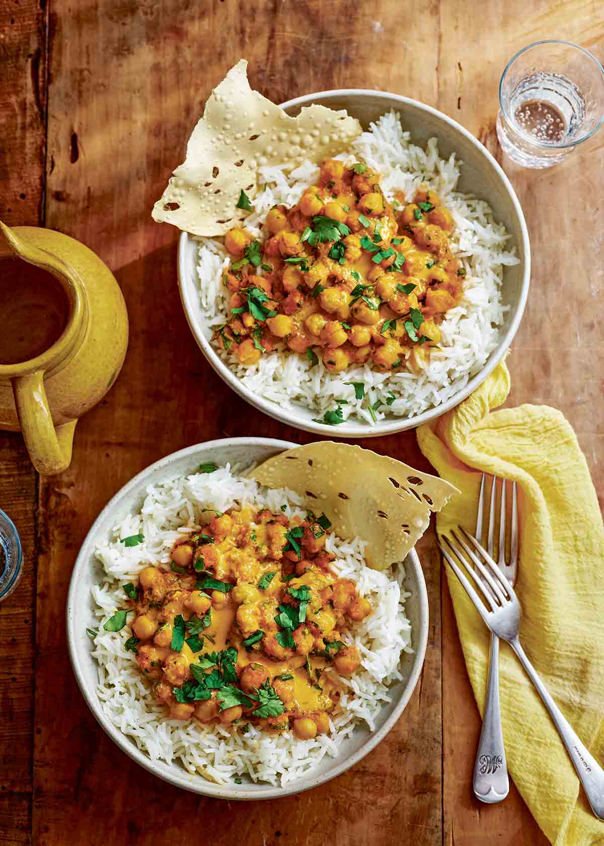 Two bowls of rice and curried chickpeas (chana masala) with two forks and a yellow cloth on the side.