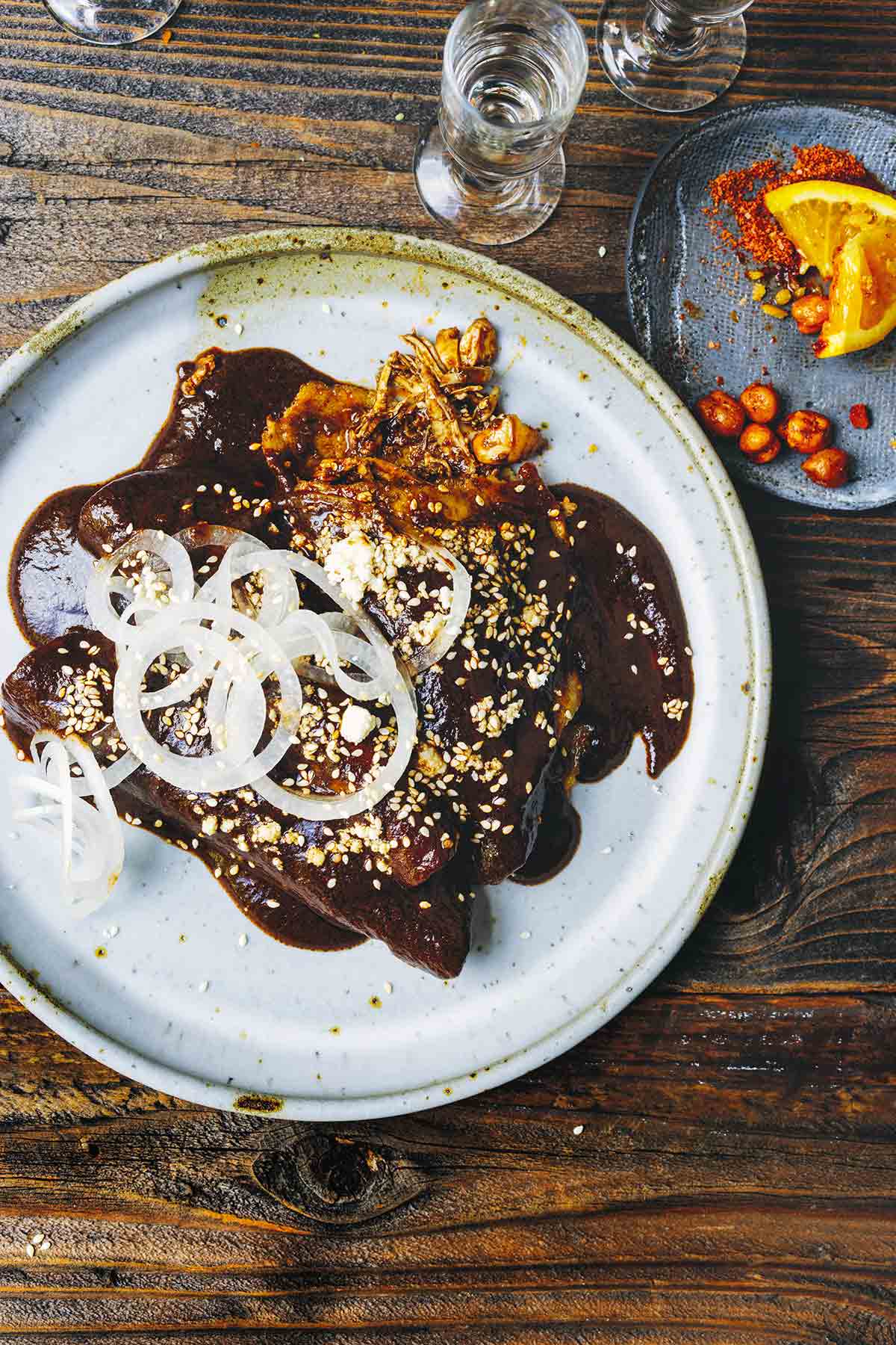 Two enchiladas de mole poblano on a white plate, topped with thinly sliced white onion.